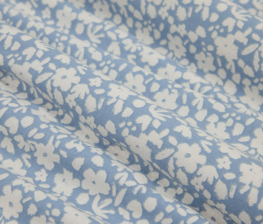 Nahaufnahme eines blauen Stoffes mit kleinen, weißen Blüten, der ein zartes und frisches Muster erzeugt.