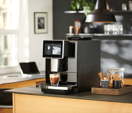 Ein Kaffeevollautomat füllt ein Glas mit Kaffee auf einer Küchentheke neben einem Glas Kekse.