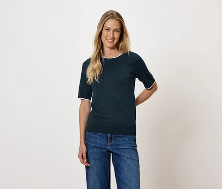 Frau mit blonden Haaren trägt ein dunkelblaues Kurzarm-Top und Jeans.