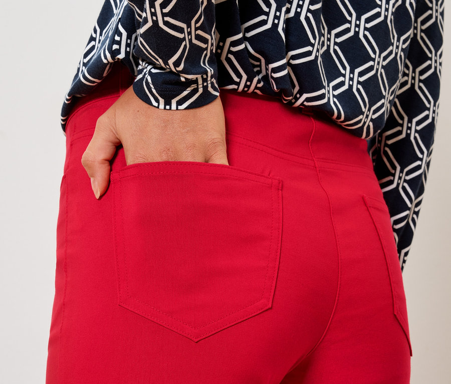 Frau steckt Hand in die Gesäßtasche einer roten Hose.