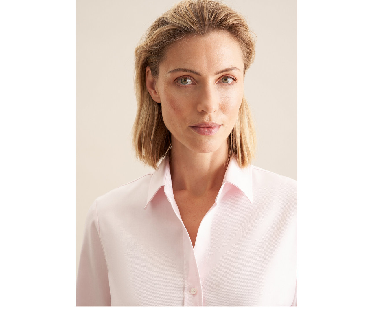 Blonde Frau trägt eine roséfarbene Seidensticker Twillbluse und blickt in die Kamera.