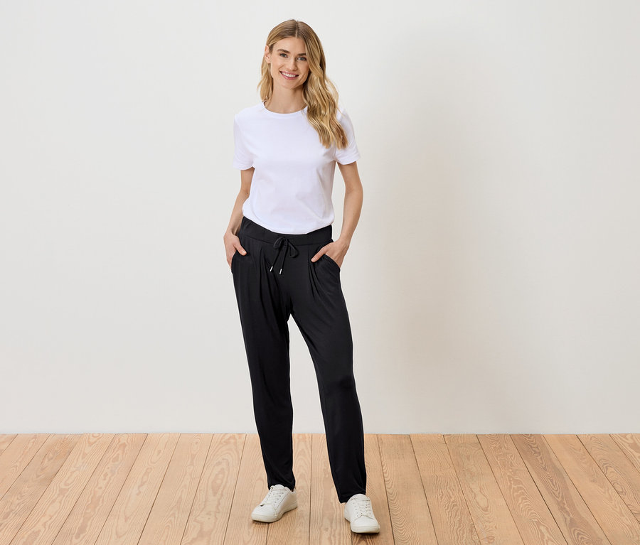 Frau mit blonden Haaren, die ein weißes T-Shirt, eine schwarze Hose und weiße Turnschuhe trägt.