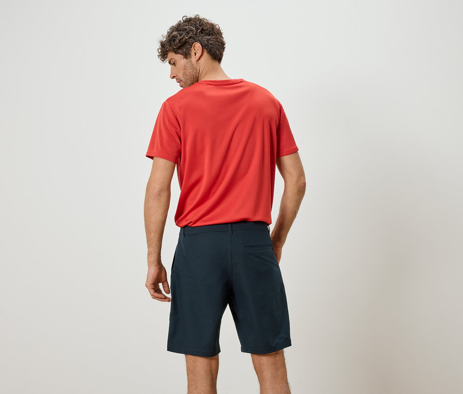 Mann von hinten, mit rotem T-Shirt und blauen Shorts vor einem weißen Hintergrund.
