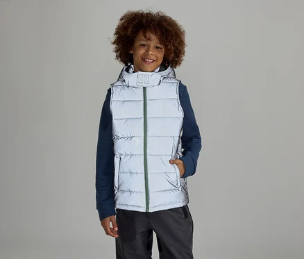 Ein Junge mit Afro steht in einer reflektierenden Weste mit Kapuze über einem blauen Pullover und grauen Hosen vor einem grauen Hintergrund.