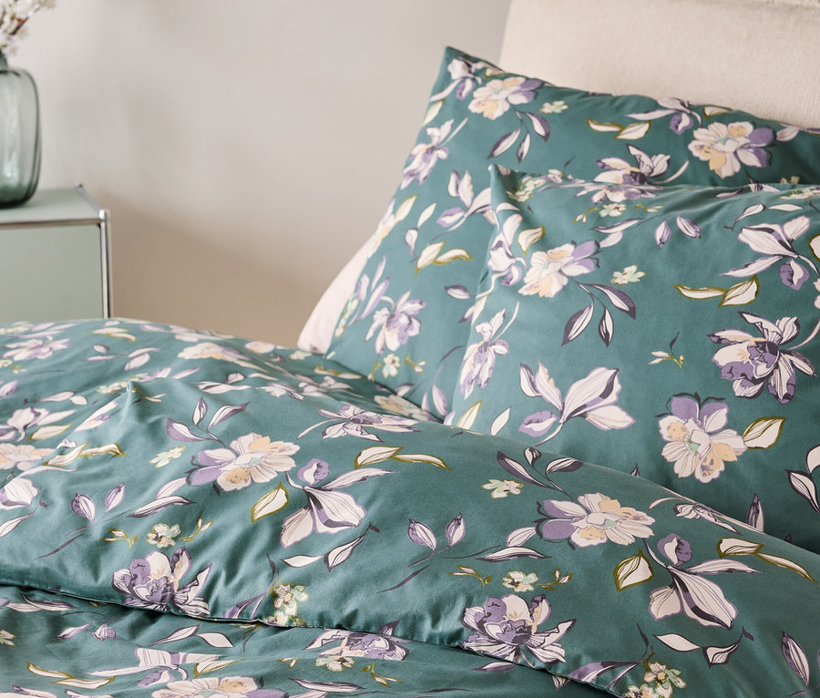 Nahaufnahme von Bettwäsche mit Blumenmuster in Grün, Lila und Weiß.