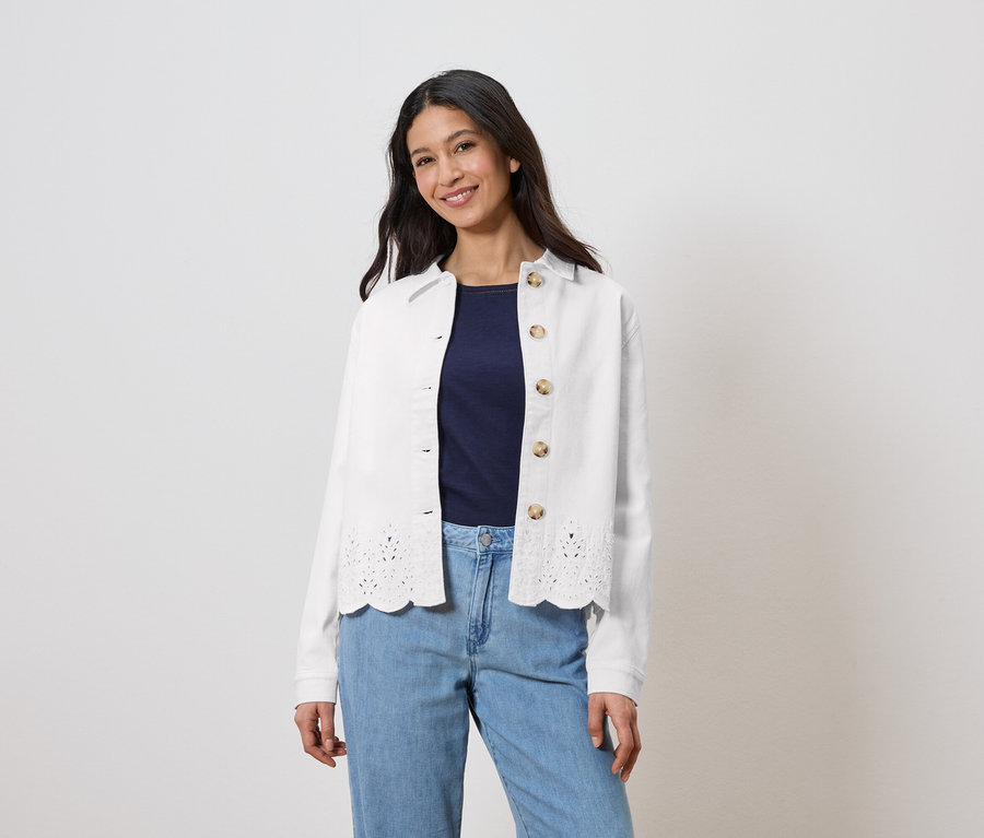 Frau trägt eine weiße Jacke mit Lochmuster über einem marineblauen Oberteil und hellblauen Jeans.