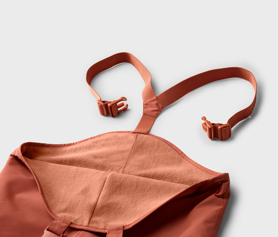Nahaufnahme einer orangefarbenen Hose mit Trägern und Schnallen auf einem weißen Hintergrund.
