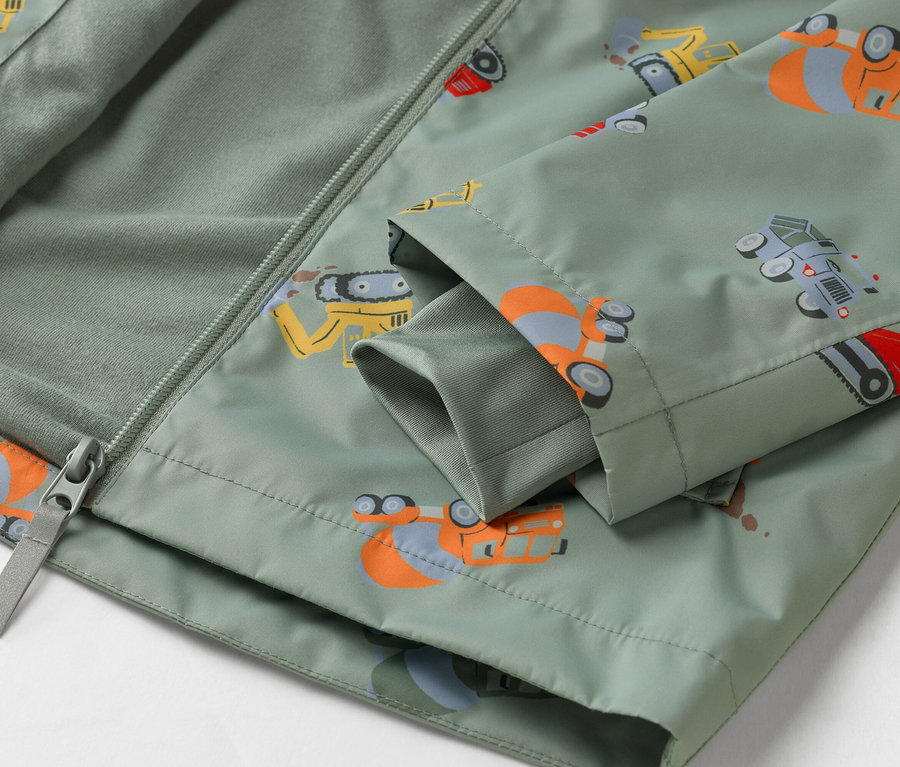 Nahaufnahme einer olivgrünen Jacke mit Baufahrzeugmuster, teilweise geöffnet mit Reißverschluss.