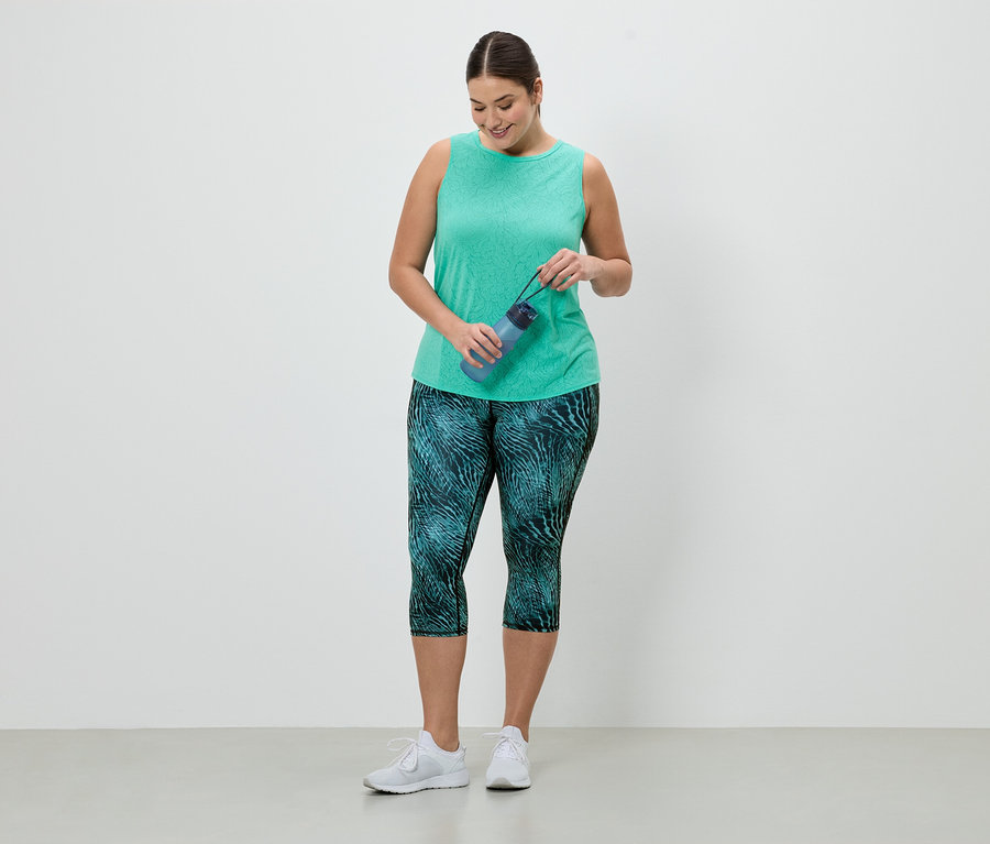 Frau im Sportoutfit hält eine blaue Wasserflasche. Sie trägt ein grünes Tanktop und Leggings mit blaugrünem Muster.