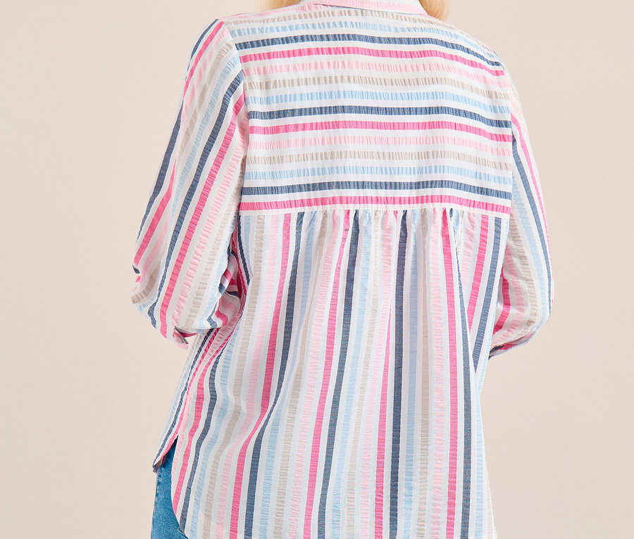Frau von hinten, trägt eine gestreifte CECIL Hemdbluse in Rosa, Blau und Weiß und blaue Jeans, blickt über ihre rechte Schulter.