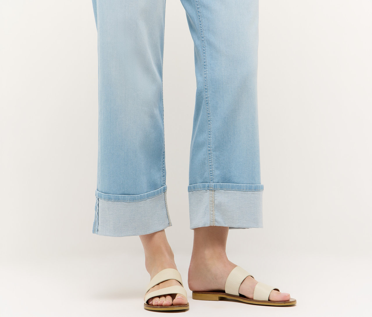 Nahaufnahme von Beinen in hellblauen Angels Denim »Laia Turn-Up« Wide Leg Jeans und Sandalen vor einem weißen Hintergrund.