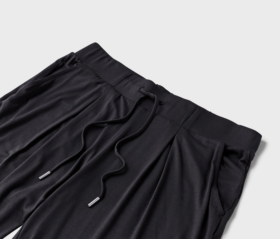 Detailansicht einer schwarzen Stoffhose mit Kordelzug und Taschen.