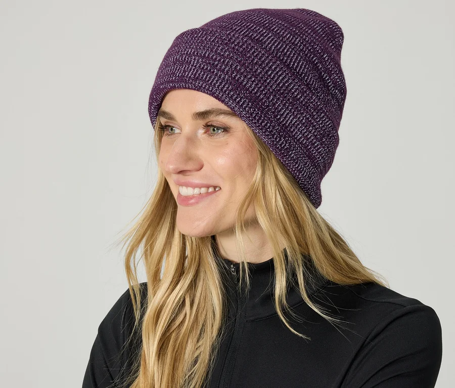 Frau mit blonden Haaren und violetter Strickmütze lächelt.