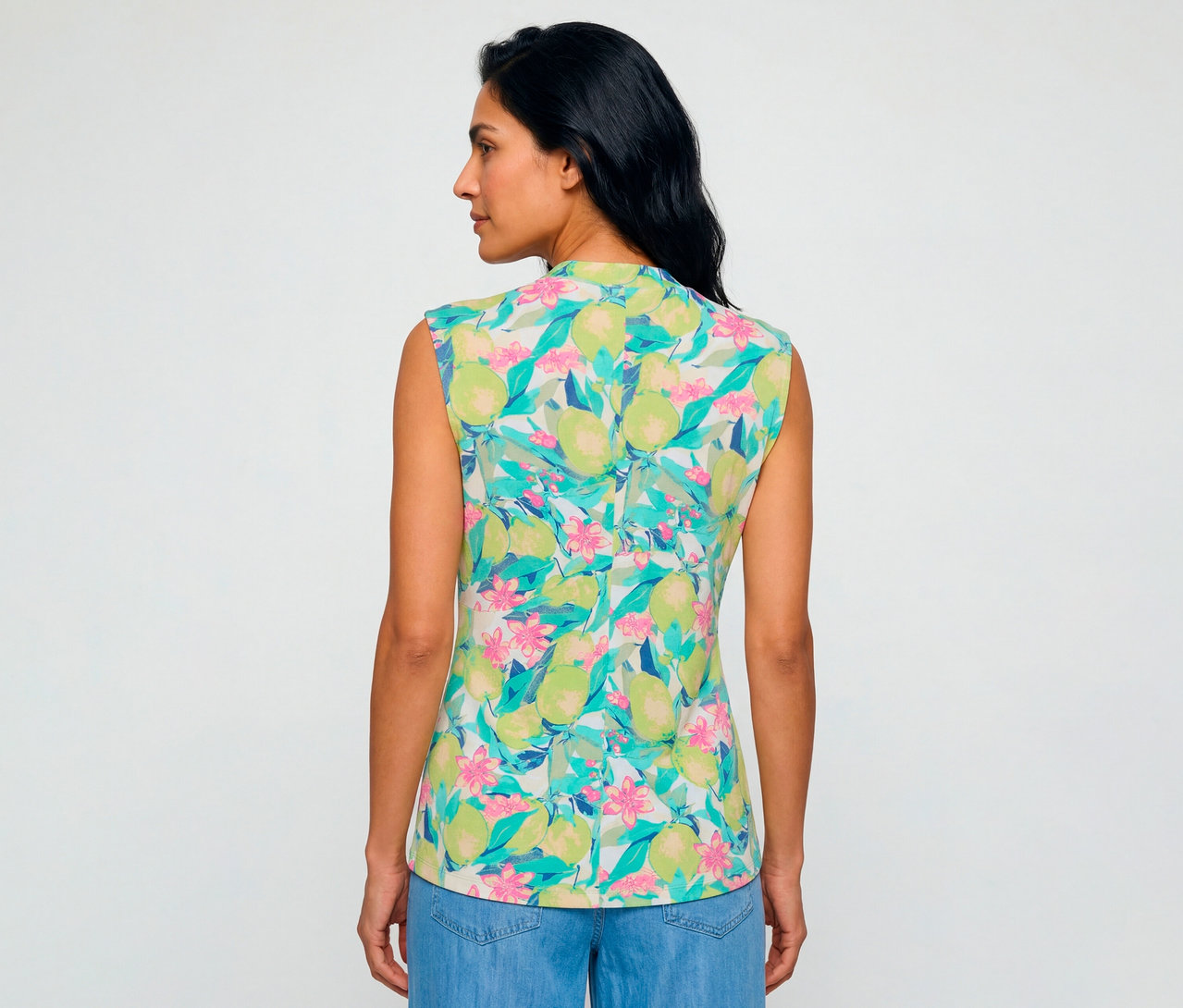 Frau von hinten, leicht zur Seite gedreht, trägt ein ärmelloses Olsen Shirt mit Limetten- und Blumenmuster zu blauen Jeans.