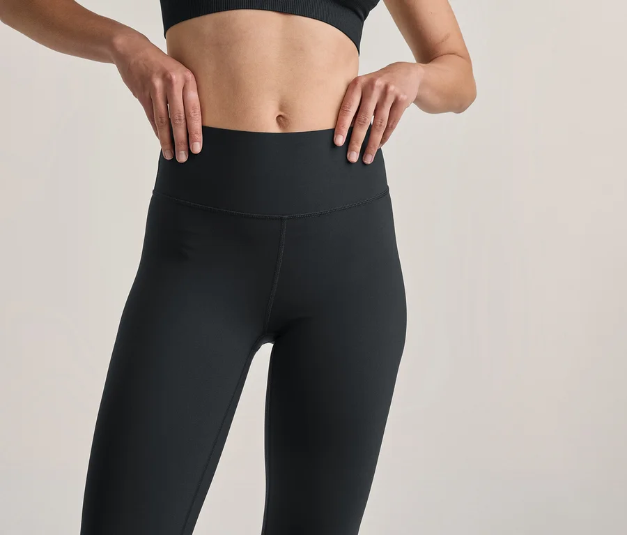 Person in schwarzen Leggings und schwarzem Sport-BH, die Hände auf die Hüften gestützt.