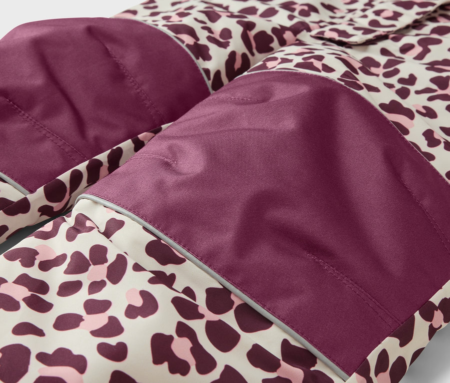 Nahaufnahme eines Kleidungsstücks mit Leopardenmuster in Beige, Dunkellila und Rosa. Es hat dunkelviolette Patches an den Knien/Ellbogen mit reflektierenden Streifen.