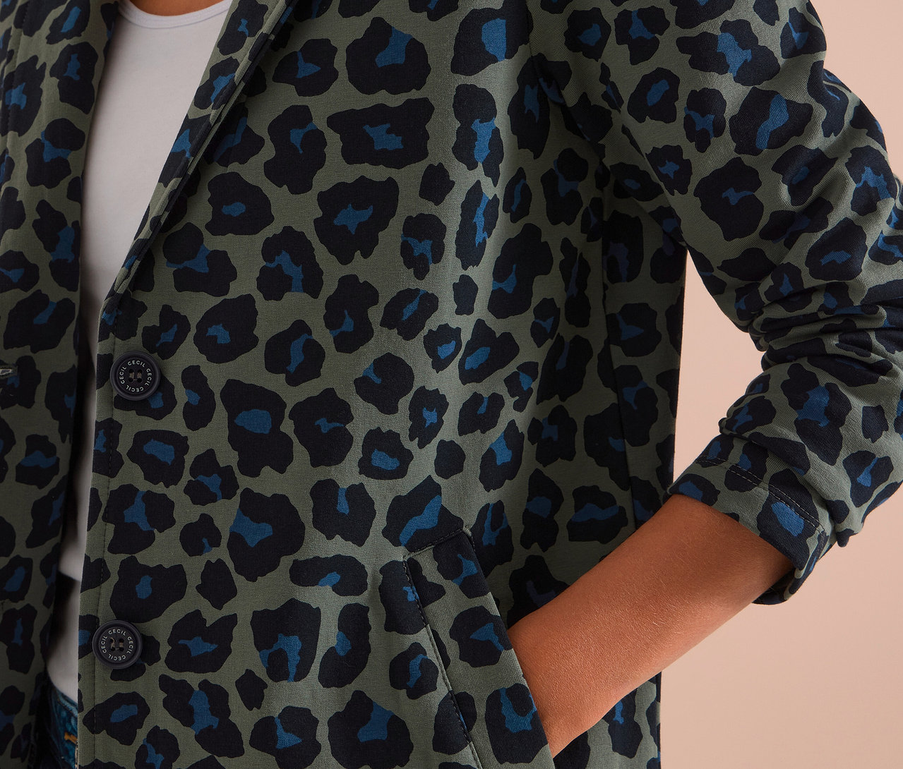 Person trägt einen CECIL Jerseyblazer mit grünem, schwarzem und blauem Leopardenmuster, die Hand in der Tasche.