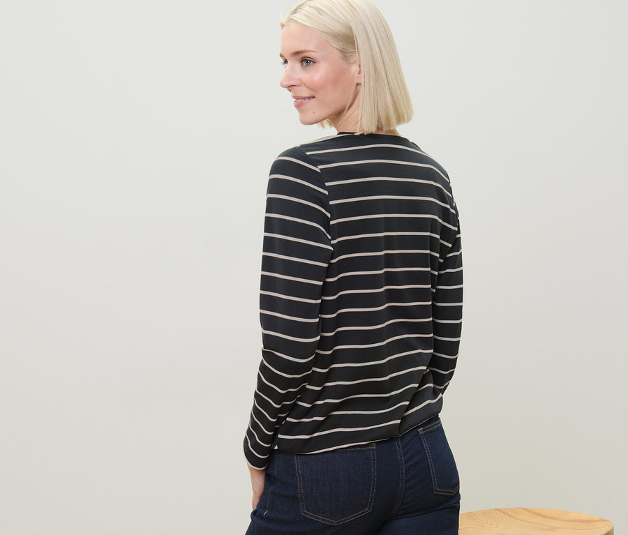 Blonde Frau blickt über die Schulter und trägt ein gestreiftes Blusenshirt aus Modal-Mix und Jeans.