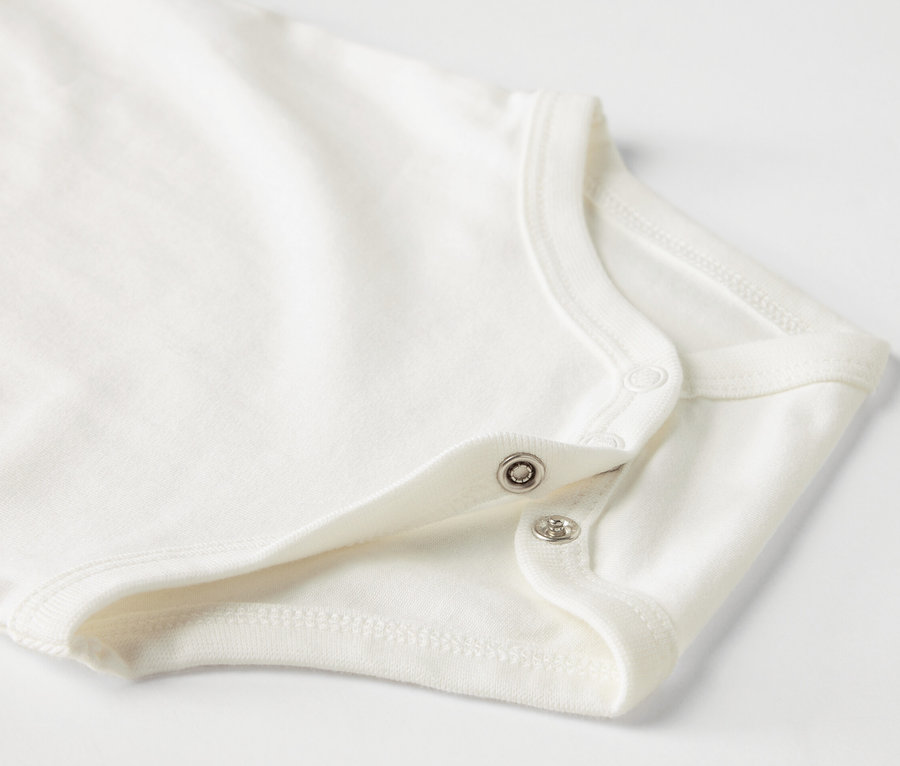 Detailaufnahme eines weißen Baby-Bodys mit kurzen Ärmeln und Druckknöpfen.