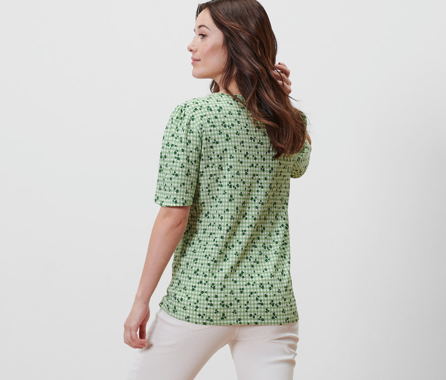 Frau posiert mit dem Rücken zur Kamera und trägt ein grünes Blusenshirt mit Alloverprint.