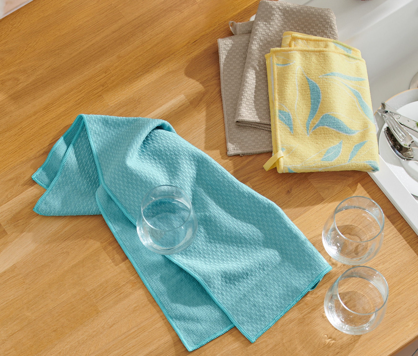 Drei Geschirrtücher und drei Gläser liegen auf einer Küchentheke.