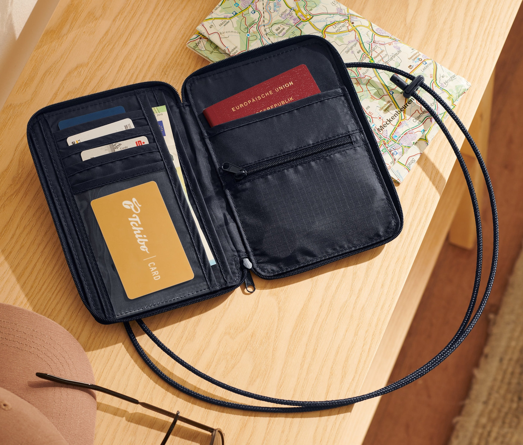 Offener schwarzer Brustbeutel mit Karten, Reisepass und Landkarte auf einem Holztisch.