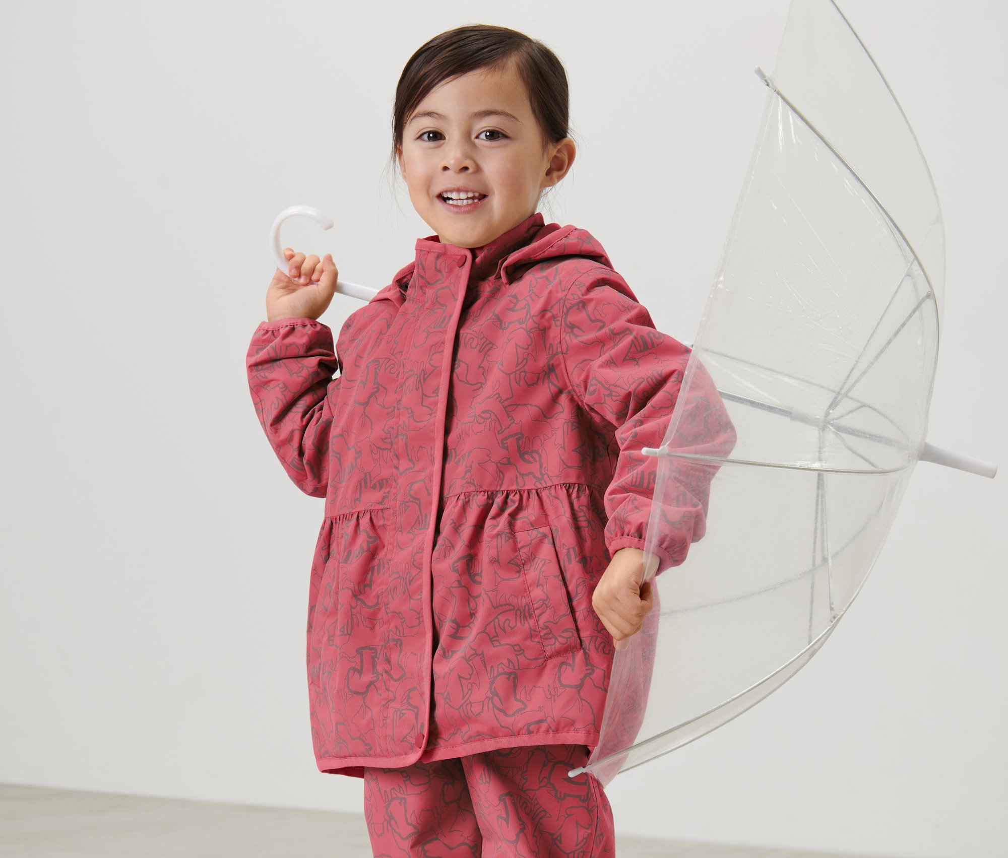 Mädchen hält einen durchsichtigen Regenschirm und trägt eine Kinder-Thermo-Regenjacke mit reflektierenden Elementen.