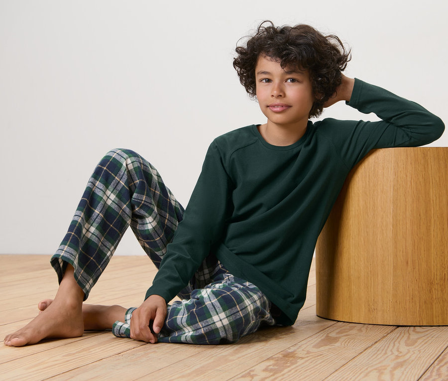 Junge sitzt auf dem Boden und lehnt sich an einen Holzhocker, er trägt einen Kinder-Flanell-Pyjama.