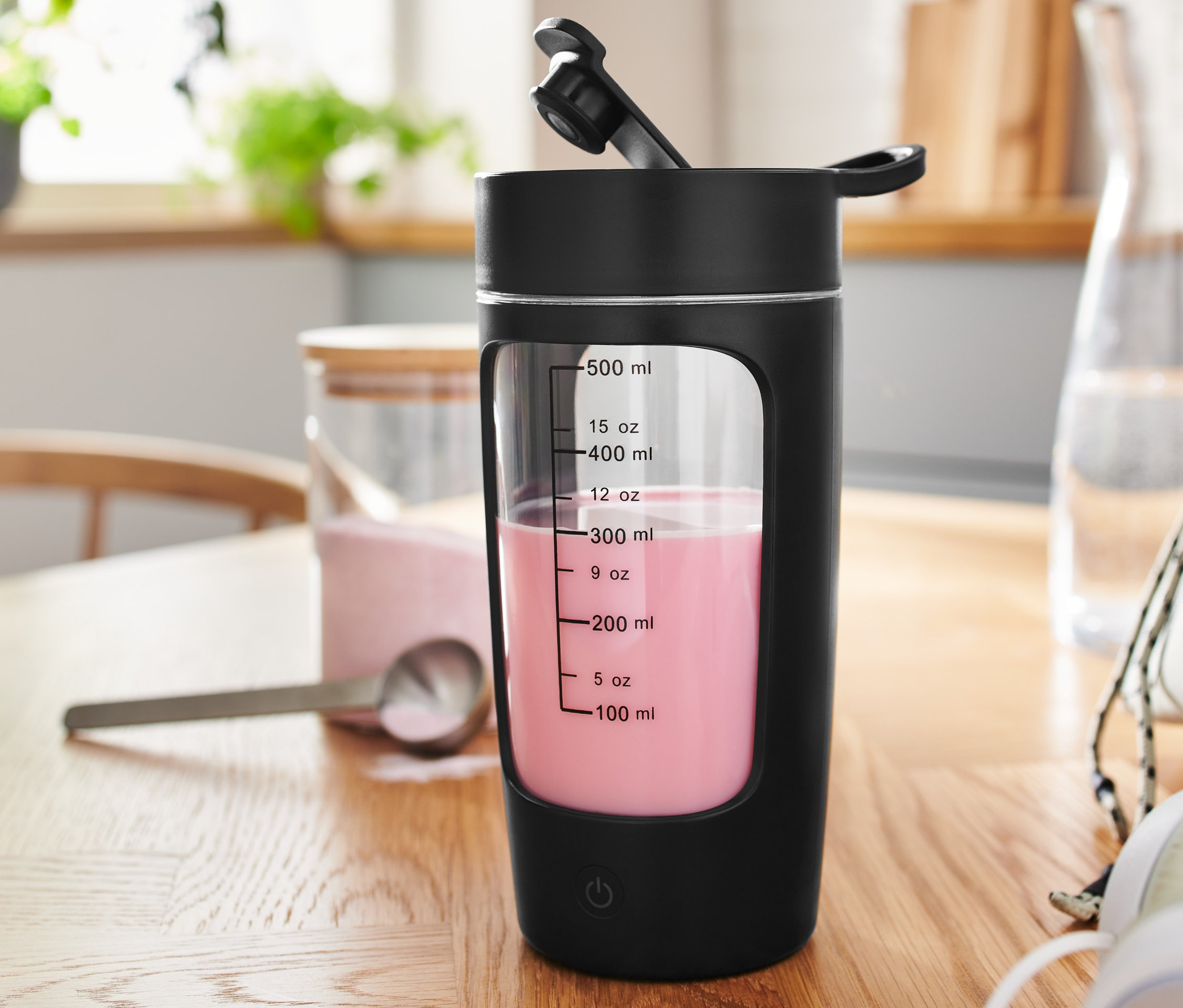 Ein schwarzer, akkubetriebener Powershaker mit rosa Inhalt steht auf einem Holztisch.