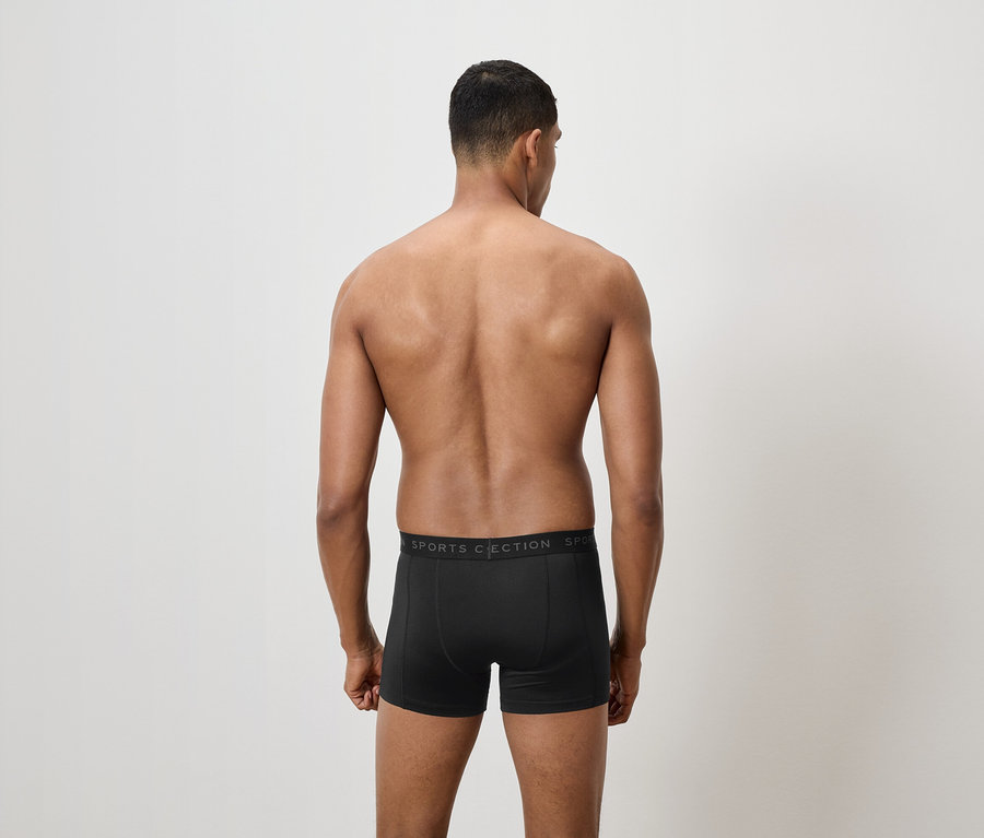 Mann mit dem Rücken zur Kamera trägt schwarze Boxershorts.