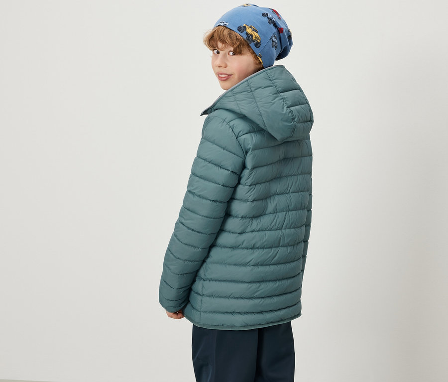 Junge mit blauer Mütze mit Autoaufdruck und grüner 2-in-1 Kinder Softshell- und Steppjacke, der über die Schulter schaut.