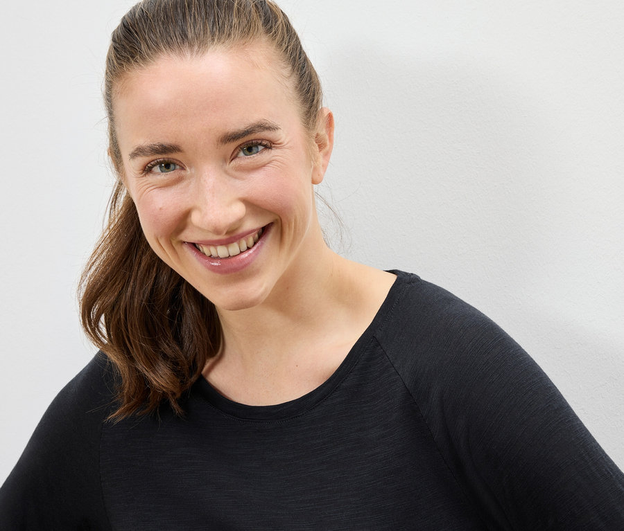Porträt einer lächelnden Frau mit braunen Haaren in einem schwarzen T-Shirt.