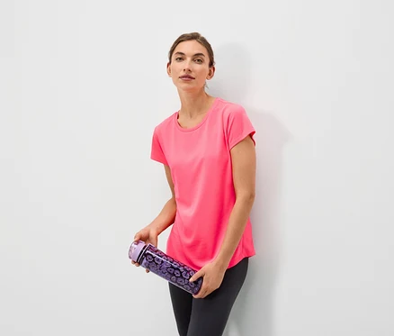Frau hält eine lila Wasserflasche mit Blumenmuster und trägt ein rosa T-Shirt und graue Leggings.