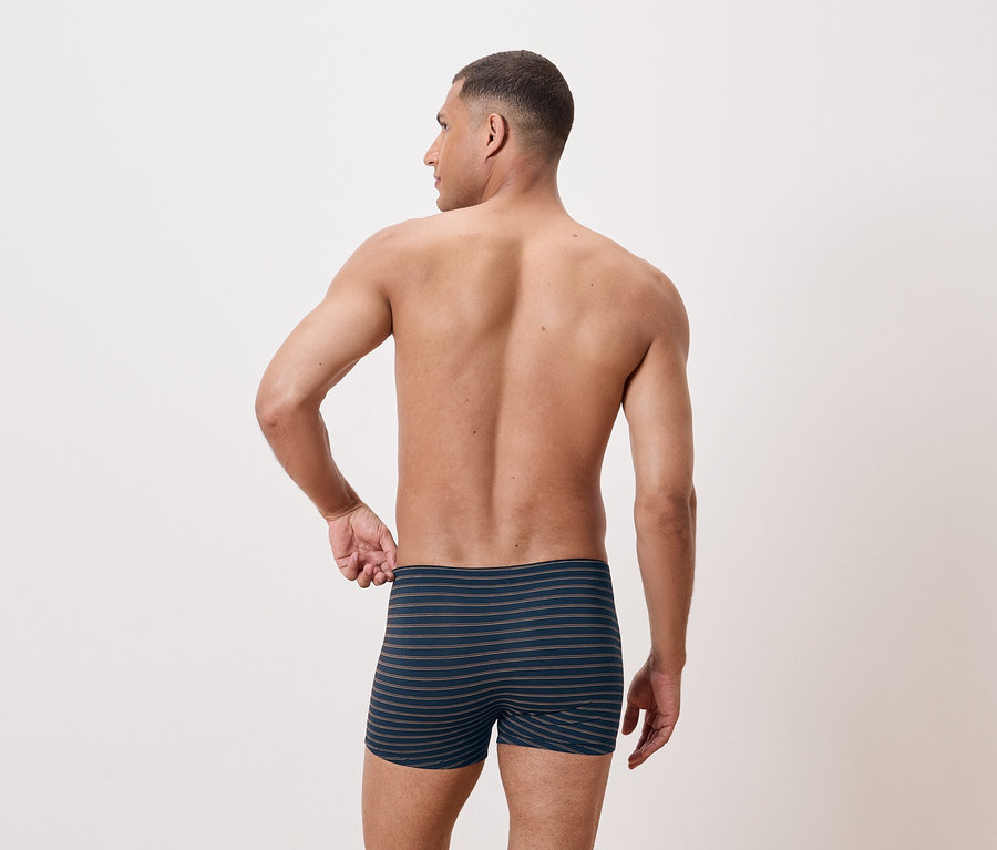 Mann mit freiem Oberkörper posiert von hinten in gestreiften Boxershorts.