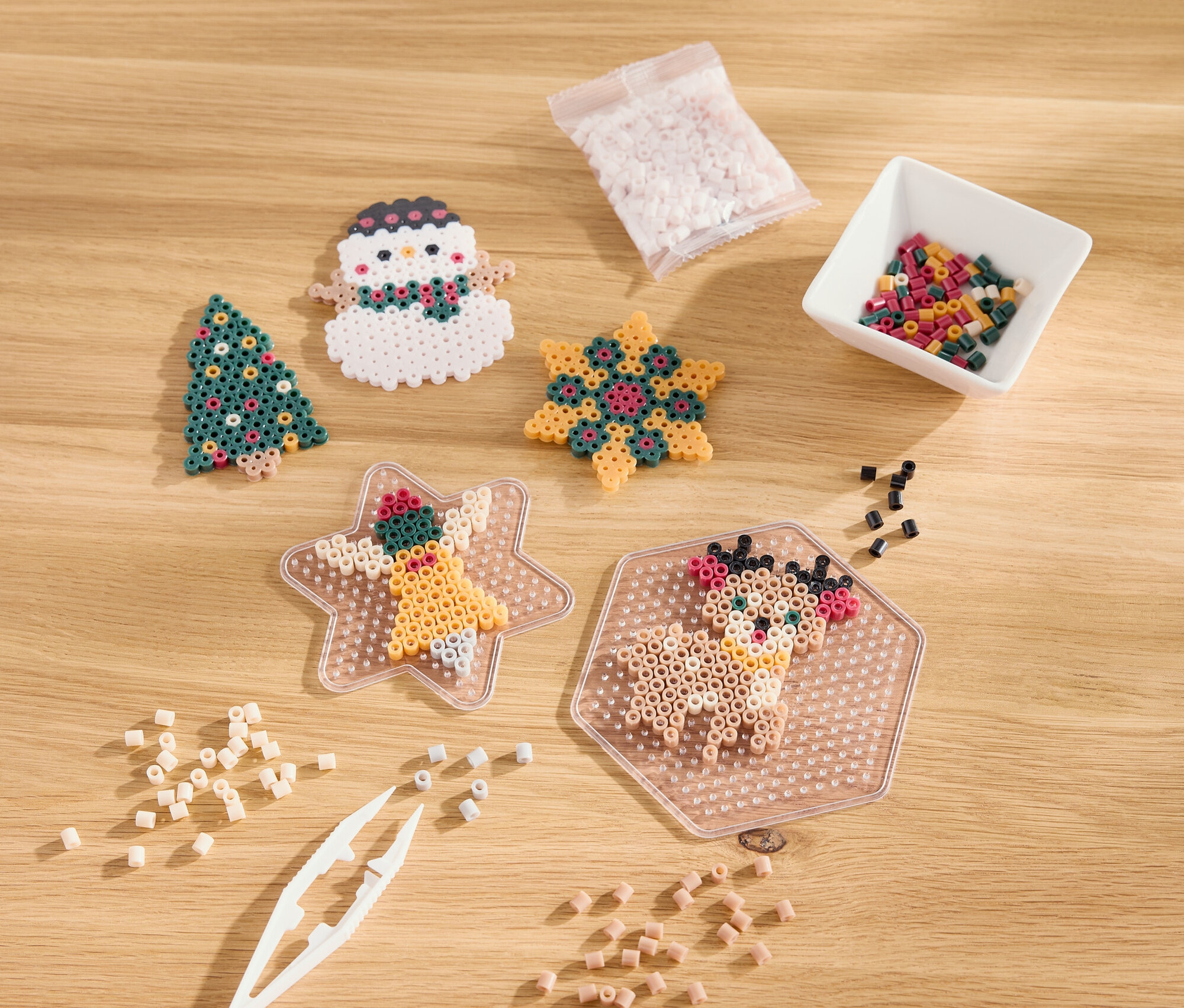 Auf einem Holztisch liegen weihnachtliche Ornamente aus Perlen, darunter ein Baum, ein Schneemann, ein Stern und ein Rentier.