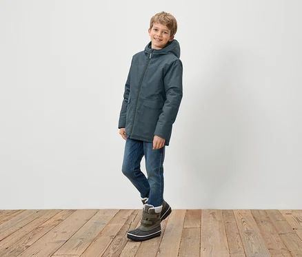 Junge posiert in blauer Kapuzenjacke, Jeans und Winterstiefeln.