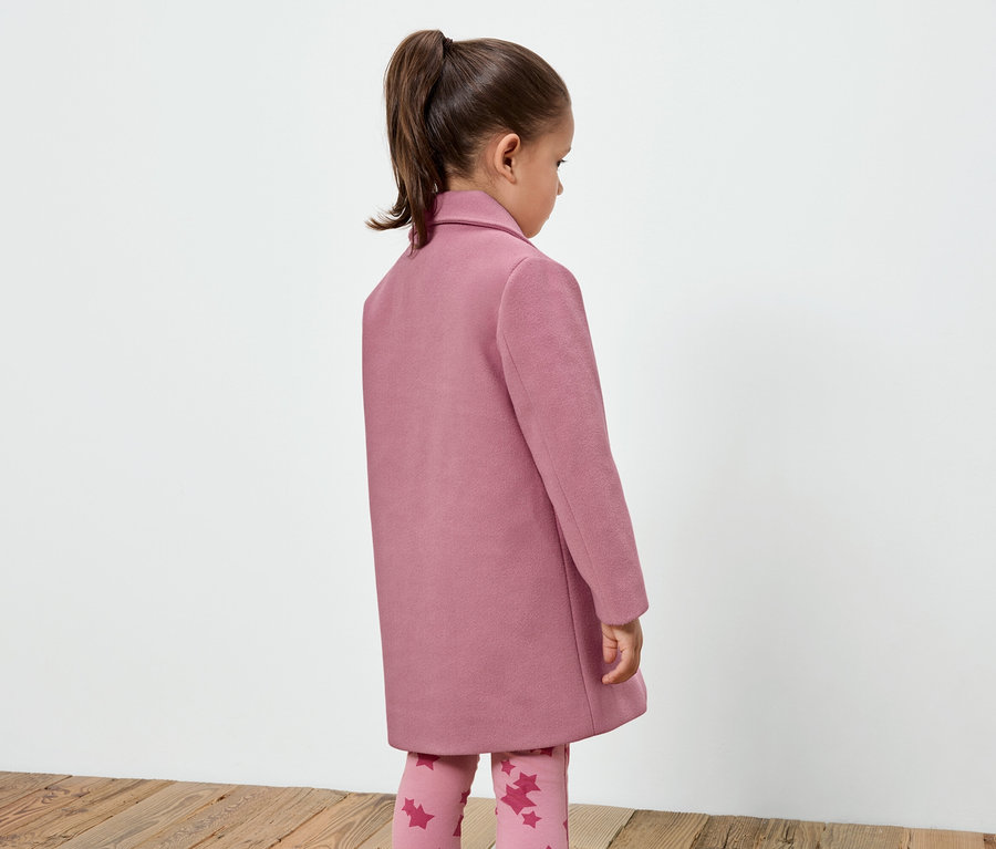 Mädchen in einem rosa Mantel und Leggings mit Sternenmuster, das mit dem Rücken zur Kamera steht.