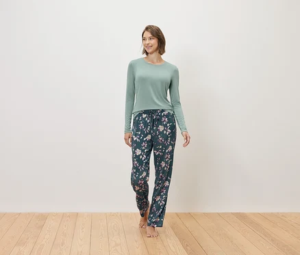 Eine Frau geht barfuß und trägt einen mintfarbenen Pullover und eine dunkelblaue Pyjamahose mit Blumenmuster.