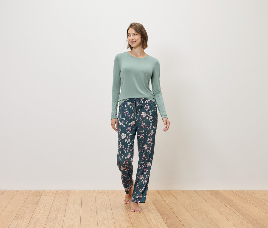Eine Frau geht barfuß und trägt einen mintfarbenen Pullover und eine dunkelblaue Pyjamahose mit Blumenmuster.