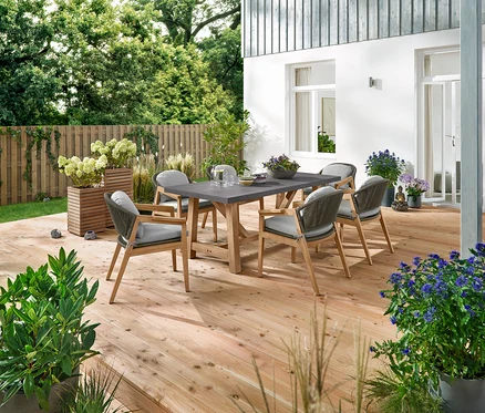 Ein Esstisch mit Polyzementplatte und sechs Komfort-Gartenstühlen mit Textilgeflecht stehen auf einer Holzterrasse. Dekorative Elemente sind 3 Solar-LED-Steine, 2 Pflanzsäulen »Tinus«, ein Buddha-Gartenbrunnen und 5 LED-Solar-Spieße.
