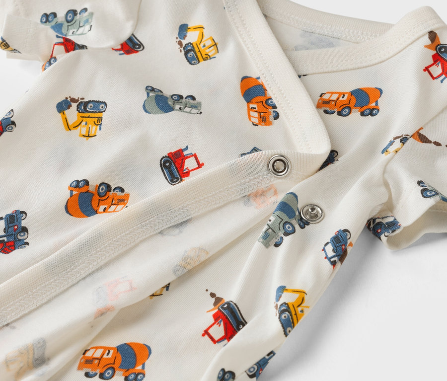 Nahaufnahme eines weißen Baby-Bodys mit Bauwagenmuster.