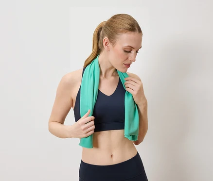 Frau mit blauem Sport-BH und Leggings hält ein türkises Handtuch um den Nacken.