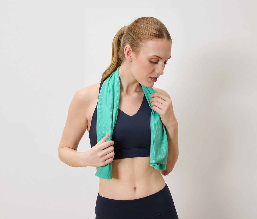 Frau mit blauem Sport-BH und Leggings hält ein türkises Handtuch um den Nacken.