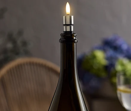 Auf einem Tisch steht eine braune Weinflasche mit einem silbernen LED-Kerzenaufsatz, der ein warmes Licht ausstrahlt.