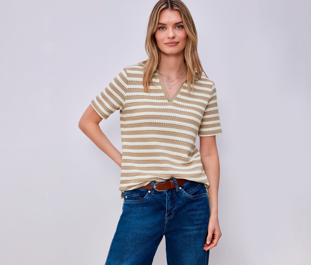 Frau mit braunem Gürtel und Jeans trägt ein gestreiftes Street One Strickshirt. Sie posiert vor einem hellen Hintergrund.