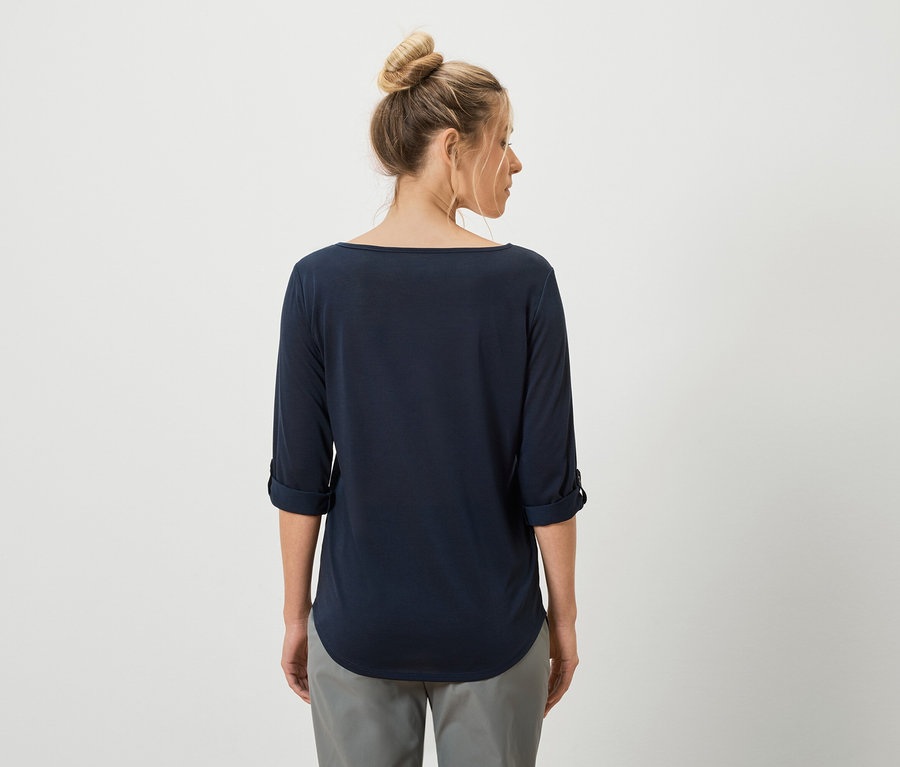 Rückansicht einer Frau mit Dutt, die ein marineblaues Langarmshirt und graue Hosen trägt.
