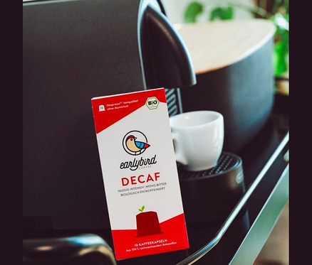 Eine Packung Earlybird Decaf Kaffeekapseln steht neben einer Kaffeemaschine und einer Tasse.