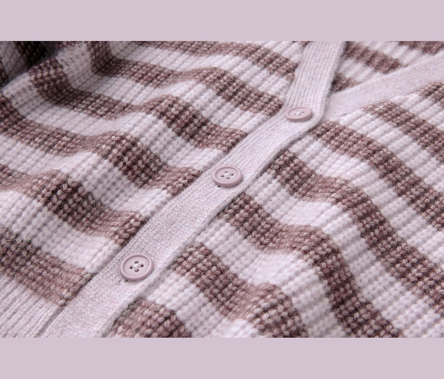 Nahaufnahme einer gestreiften Strickjacke mit hellbeigen und braunen Querstreifen und einer Knopfleiste mit drei hellvioletten Knöpfen.