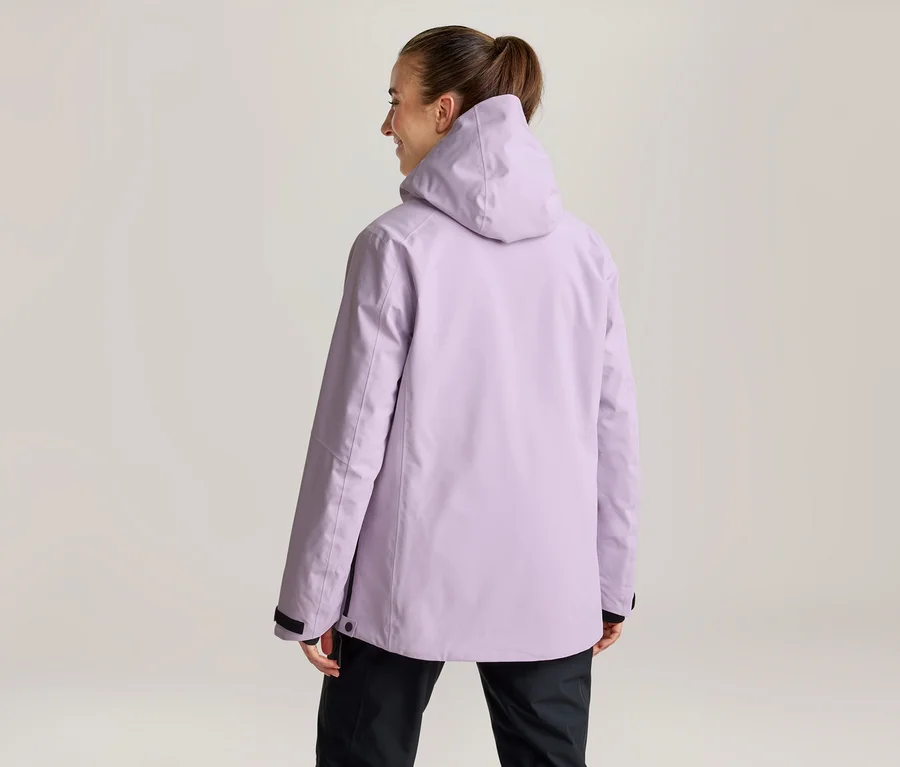 Frau von hinten, trägt eine hellviolette Kapuzenjacke und schwarze Hose, Haare zum Pferdeschwanz gebunden, blickt nach rechts.