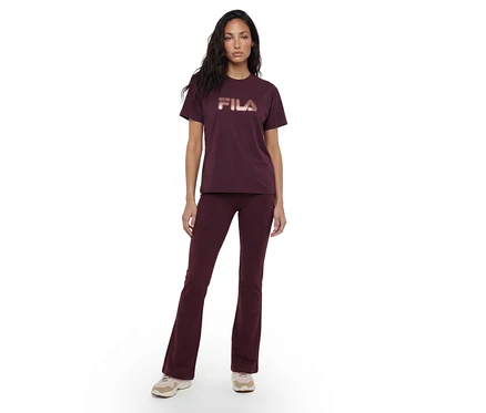 Eine Frau steht frontal, trägt ein dunkelrotes T-Shirt mit roségoldenem „FILA“-Logo und dazu passende dunkelrote Schlaghosen, kombiniert mit hellen Sneakern.